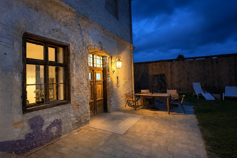 Außenbereich der Ferienwohnung in der alten Volksschule Gaas bei Abendlicht mit historischem Eingang, Terrasse und Garten