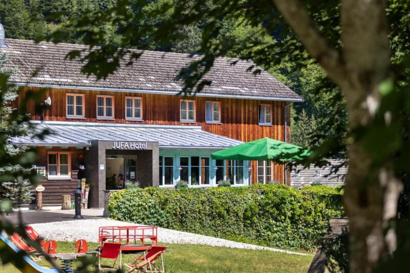 JUFA Hotel Eisenerzer Ramsau mit Holzfassade, Hoteleingang und Spielbereich im Grünen