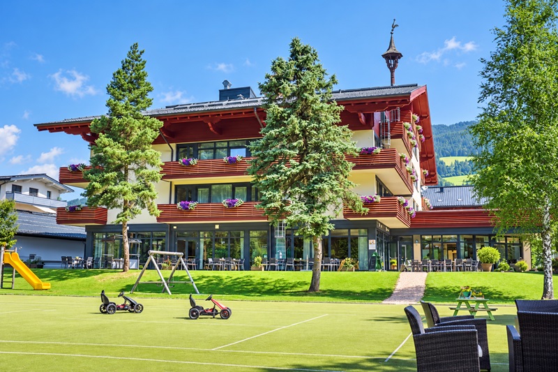 JUFA Hotel Altenmarkt mit roten Holzbalkonen, Terrasse und Spielbereich im Garten